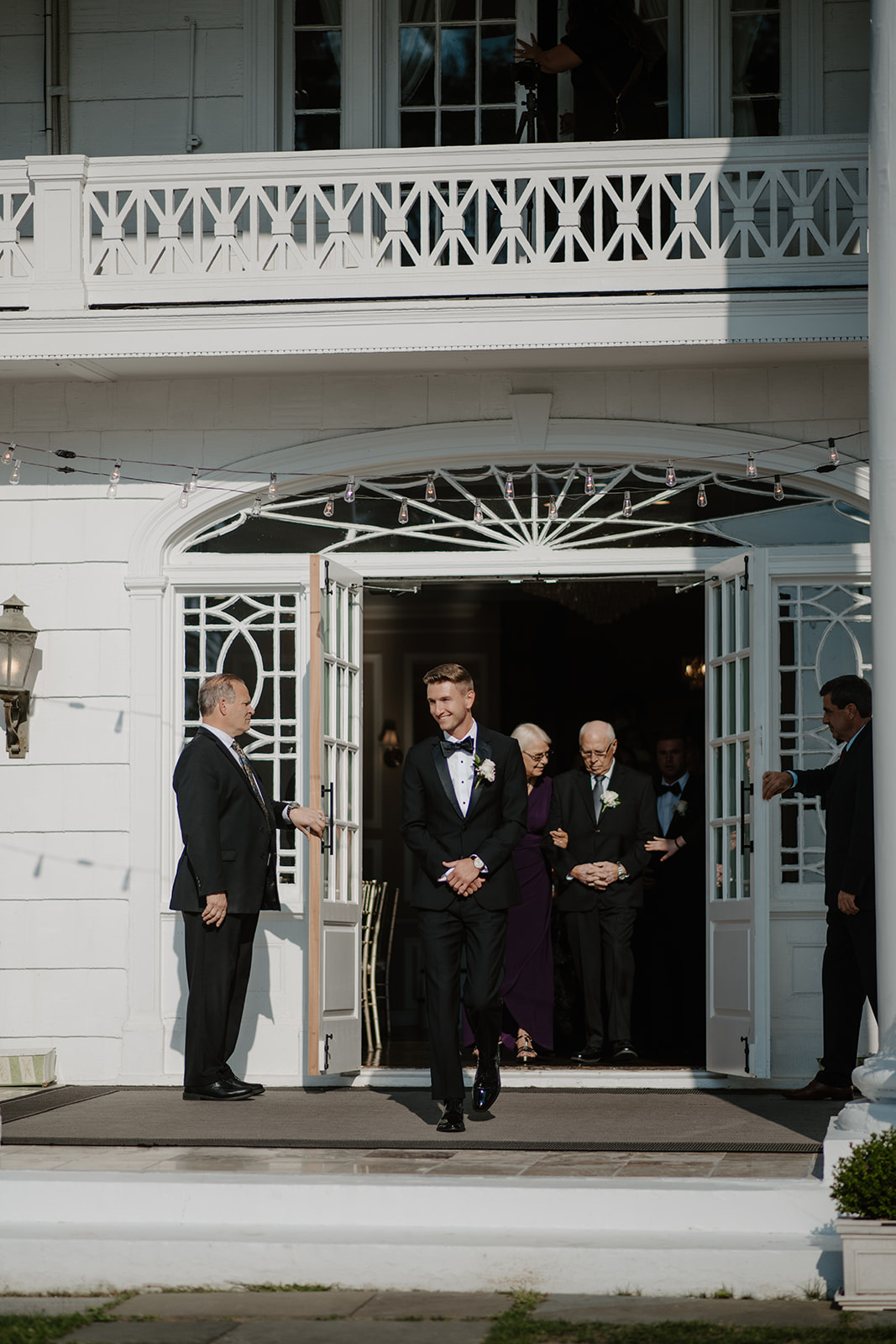 Groom smiles as he walks out of the white double doors of the manor to begin the wedding processional.